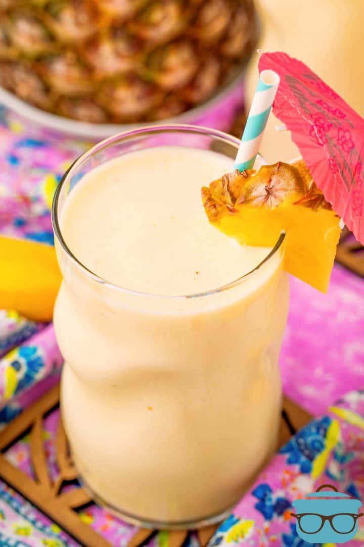 Overhead photo of pineapple smoothie in a glass with pineapple, straw and a pink drink umbrella.