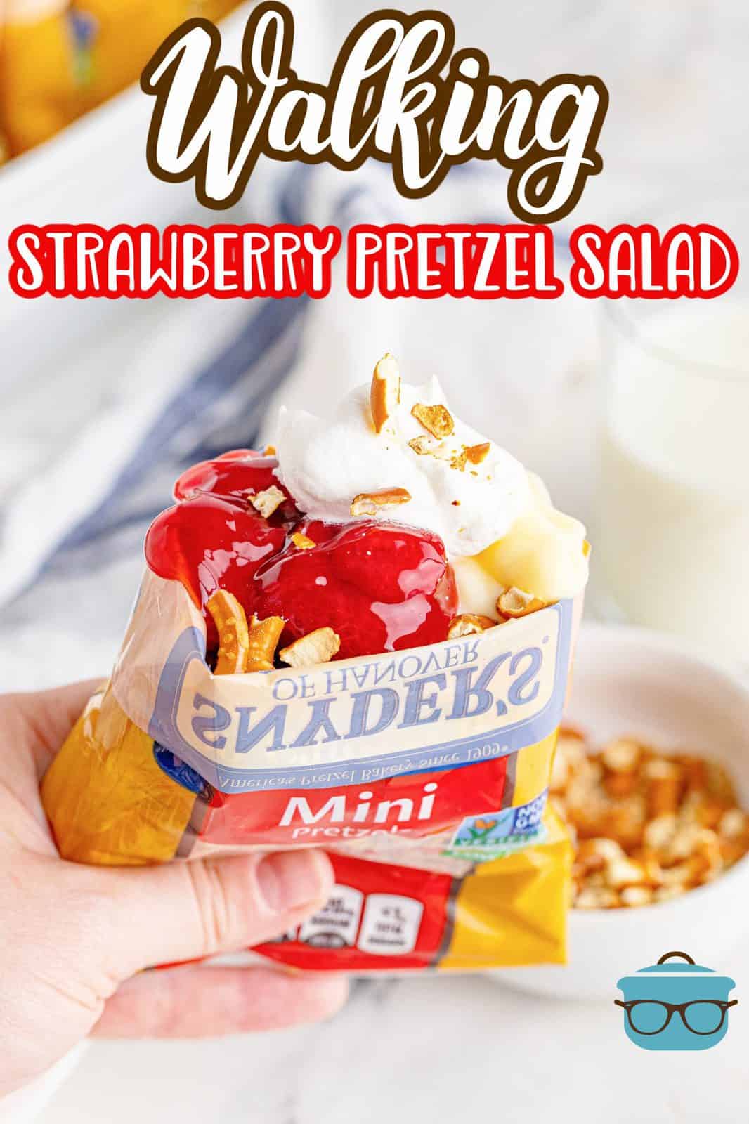 Photo of a hand holding a pretzel bag filled with Walking Strawberry Pretzel Salad by The Country Cook. 