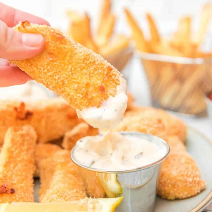 Square image of Air Fryer Homemade Fish Sticks close up with hand holding a dipped fish stick