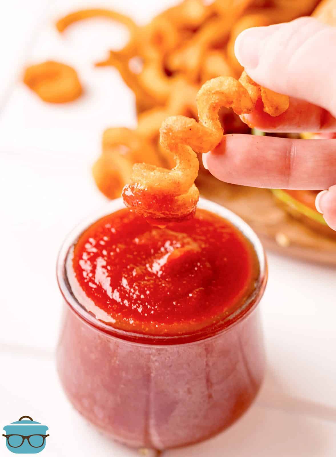 Hand dipping curly fry in Homemade Ketchup.