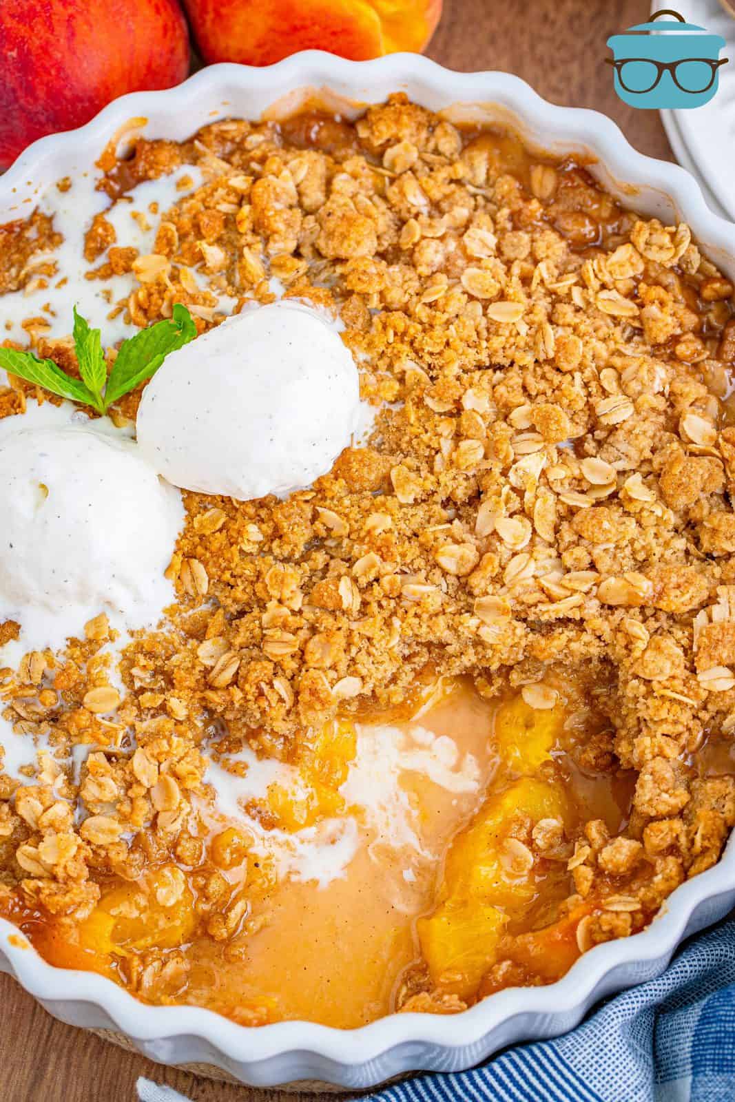 Overhead of Peach Crisp in baking dish with ice cream on top with some crisp removed.