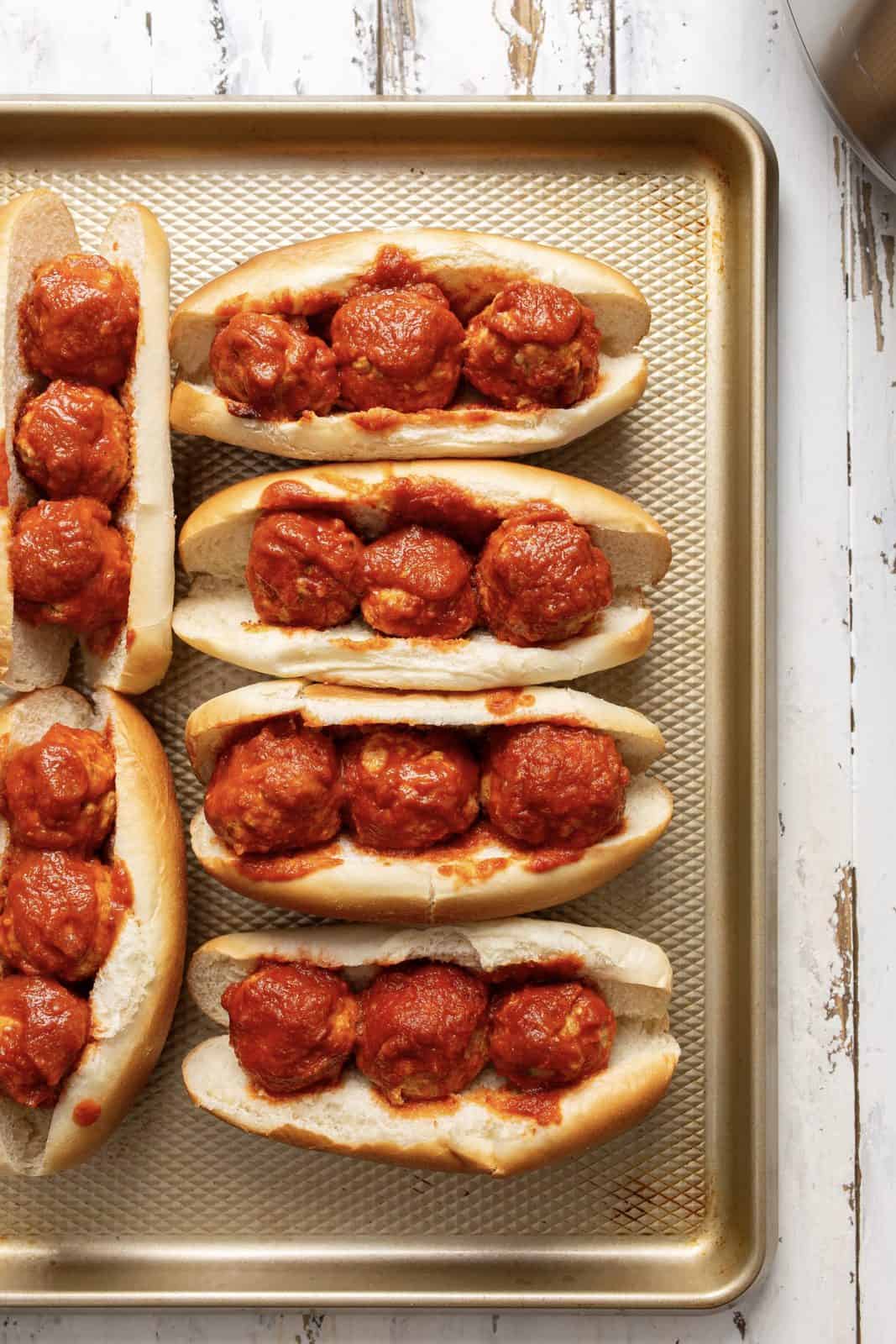 Meatballs placed on sub buns on baking sheet.