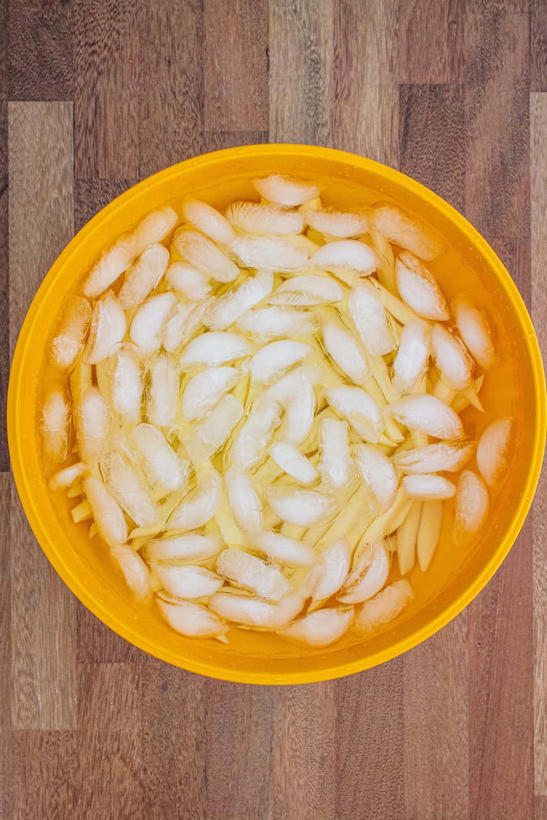 sliced uncooked French fries soaking in an ice water bath