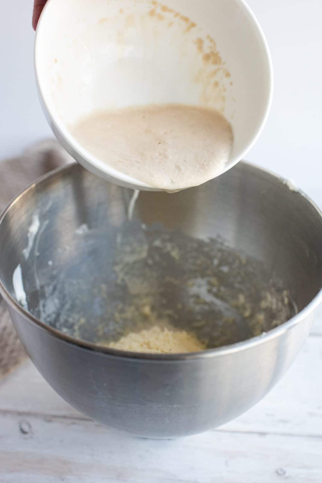 Yeast mixture being added to butter and sour cream mixture in bowl of stand mixer.