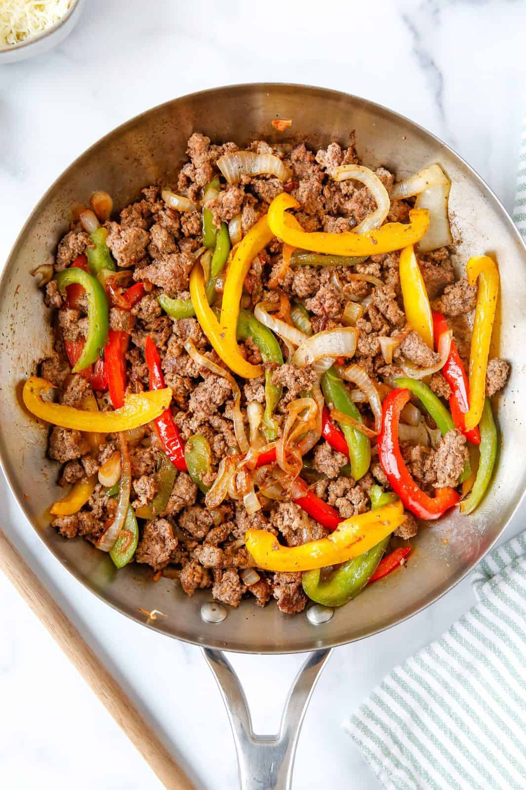 Beef mixed into skillet with sliced peppers and onions.