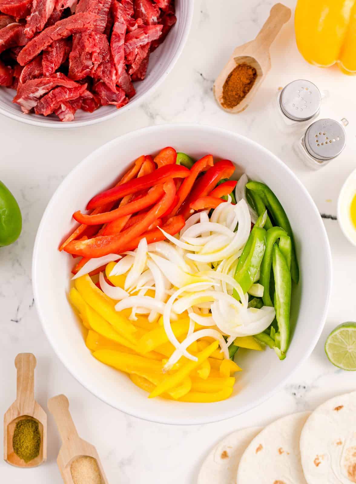 Sliced peppers in onions in white bowl.
