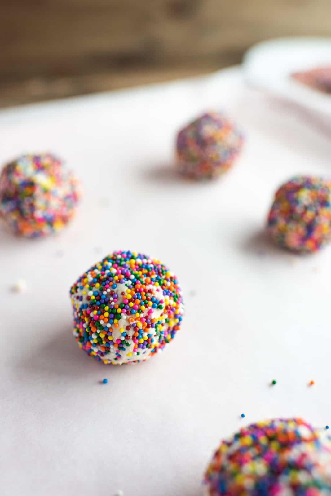 Cookies rolled in nonpareils on parchment paper lined baking sheet.