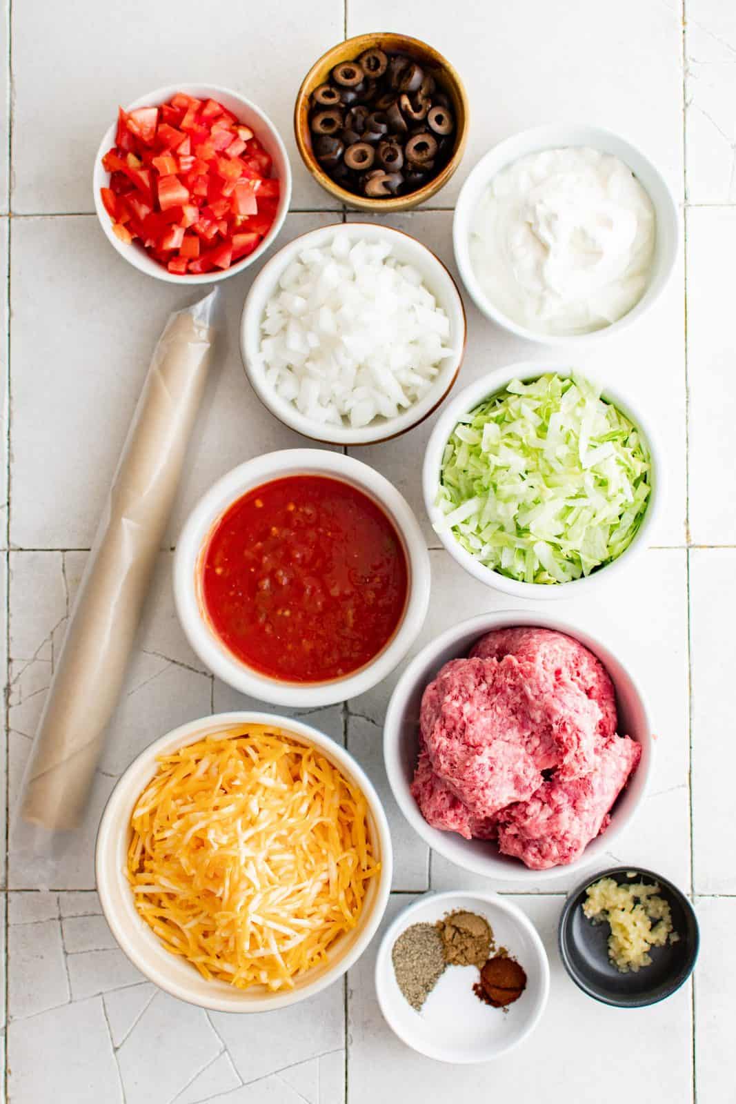 Ingredients needed: premade pie crust, ground beef, white onion, garlic, salt, black pepper, cumin, chili powder, Colby Jack cheese, salsa, sour cream, shredded iceberg lettuce, tomatoes and black olives.  