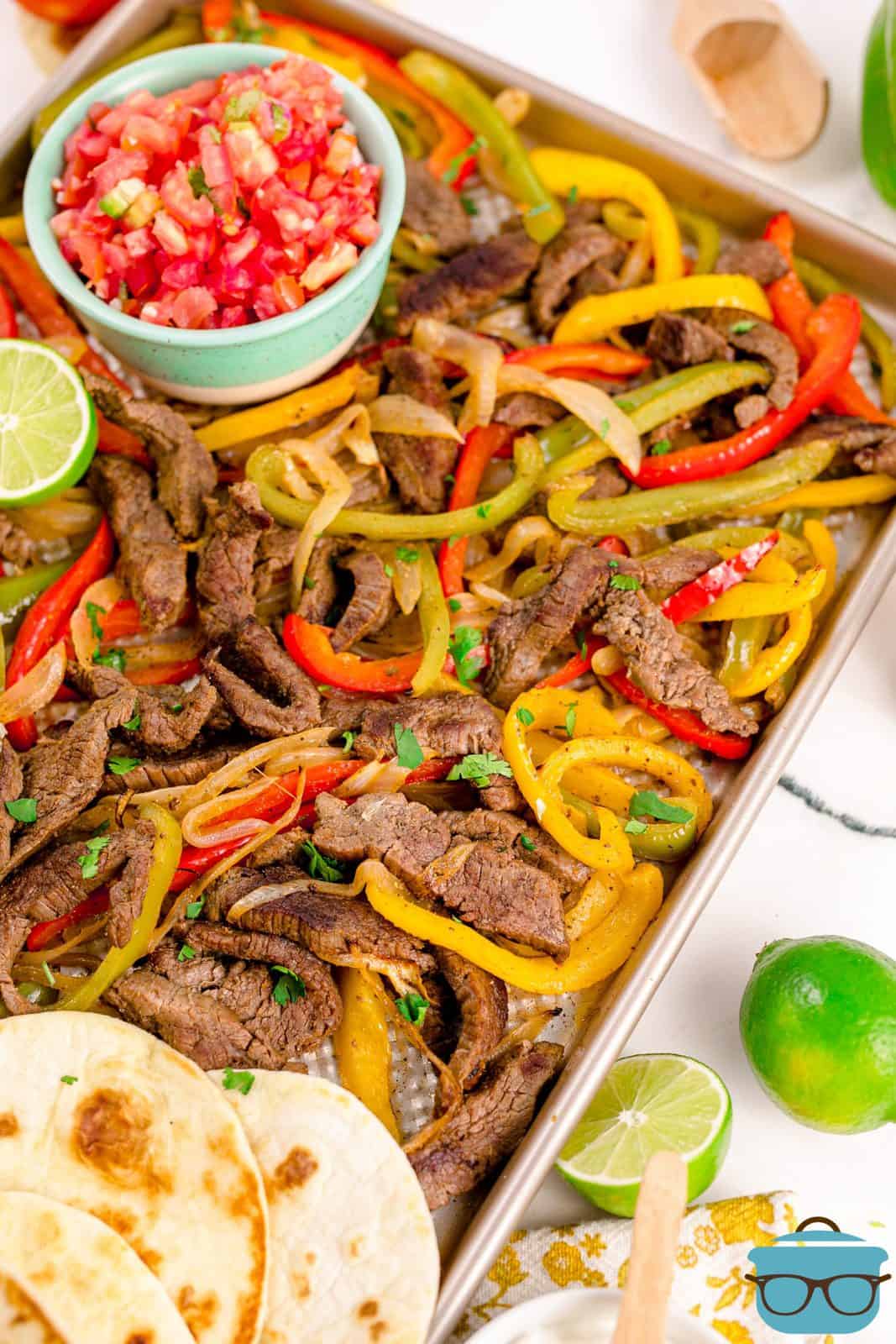 Finished Sheet Pan Beef Fajitas on pan with toppings and tortillas.
