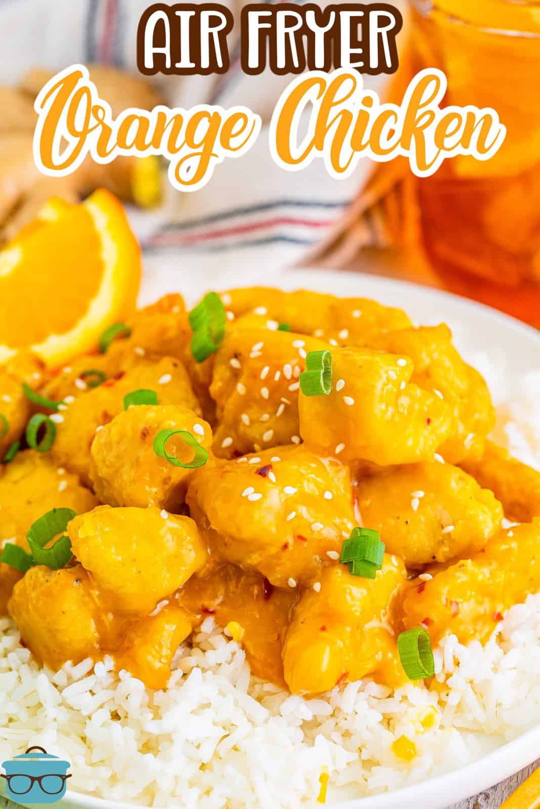 pieces of orange chicken shown in white rice with a slice of fresh orange on the side.