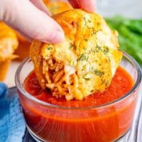Square image of hand dipping one Spaghetti Cup into sauce.