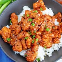 Square image of Easy General Tso's Chicken over white rice with sesame seeds and scallions.