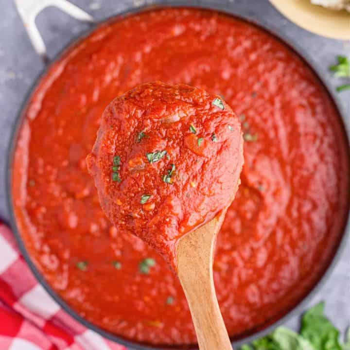 Square image of wooden spoon holding up a scoop of Homemade Marinara Sauce