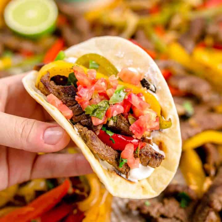 Squarer image of hand holding fajitas in a tortilla.