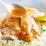 Square image of spoon dripping gravy over chicken on plate.