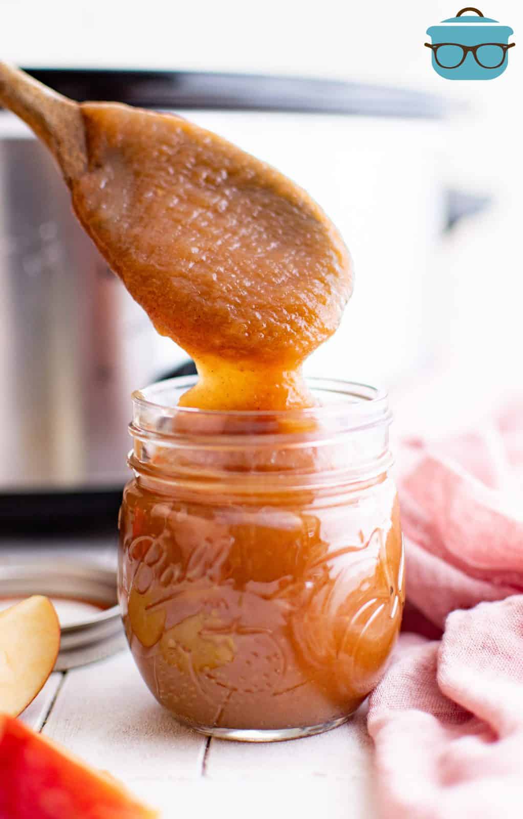Wooden spoon putting Slow Cooker Apple Butter in glass jar.