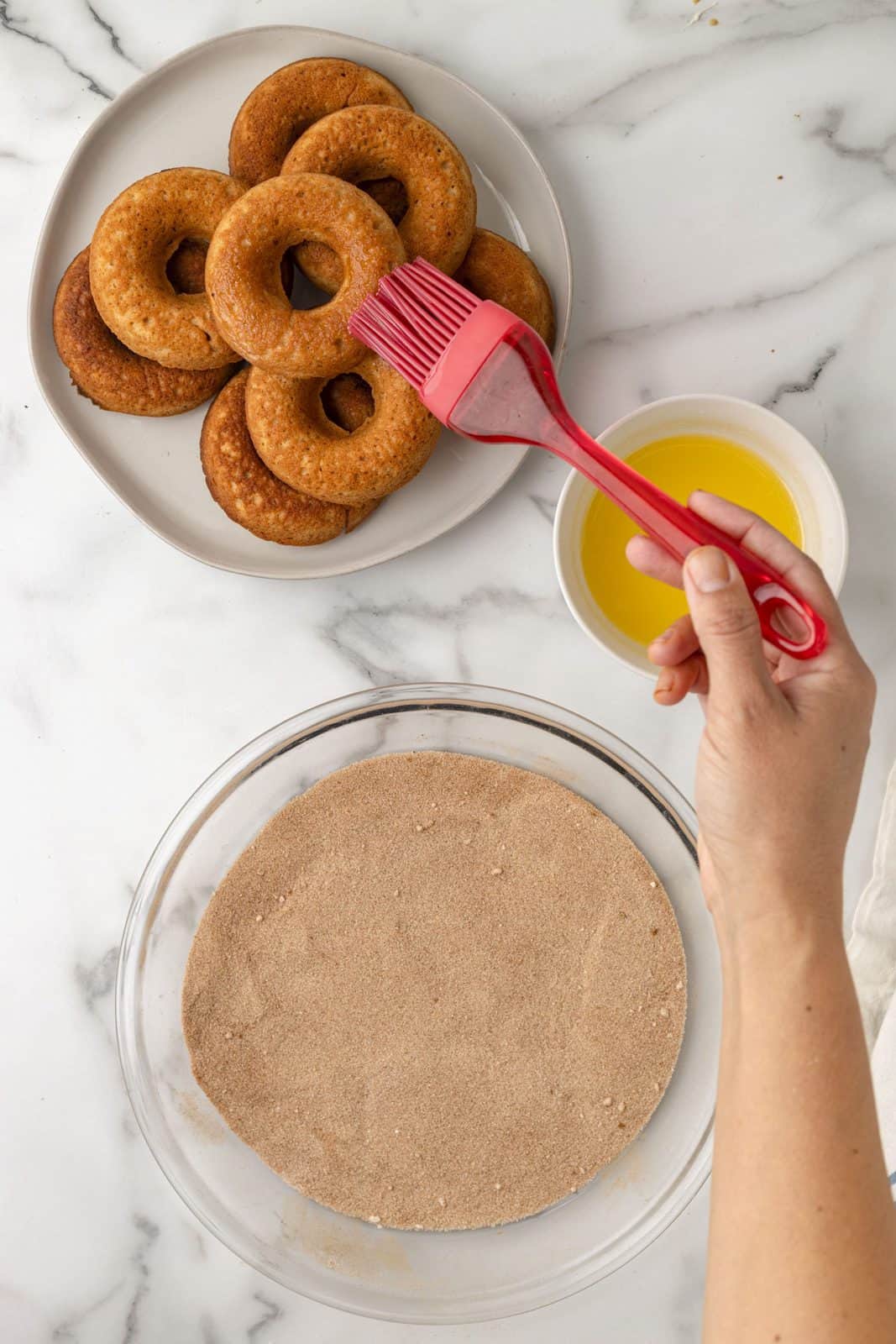 Mixed up cinnamon sugar in bowl and hand brushing donut with melted butter.
