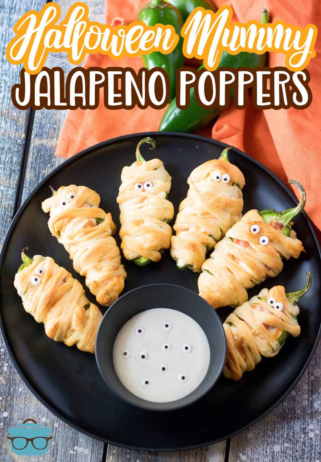 Pinterest image of finished Halloween Mummy Jalapeno Poppers on black plate with dipping sauce.