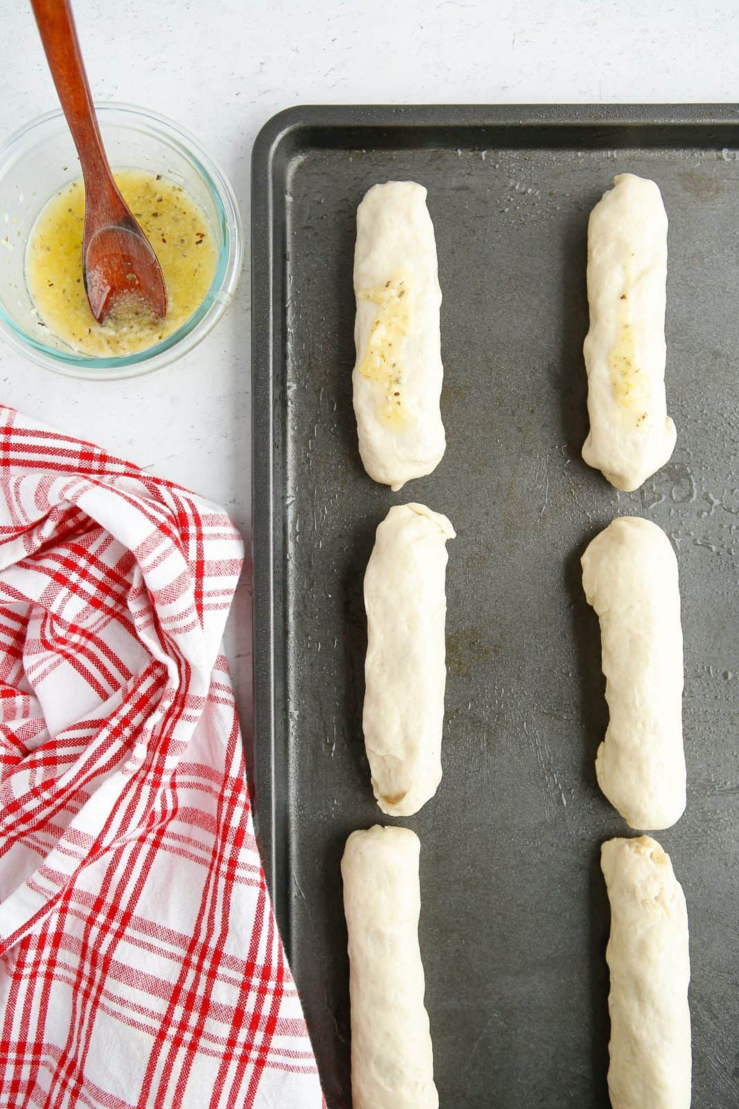 Wrapped up Pizza Roll Breadsticks on baking sheet brushed with garlic butter sauce.