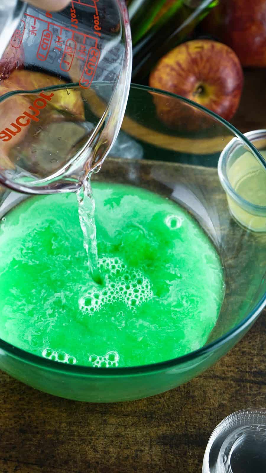 Vodka and lime juice being added to jell-o mixture in bowl.