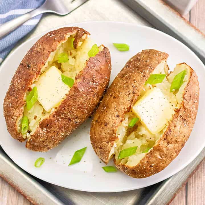 Square image of two Air Fryer Baked Potatoes with butter and green onions on white plate.
