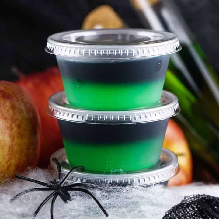 Square image of two stacked Halloween Poison Apple Jell-O Shots with fake spider and web.