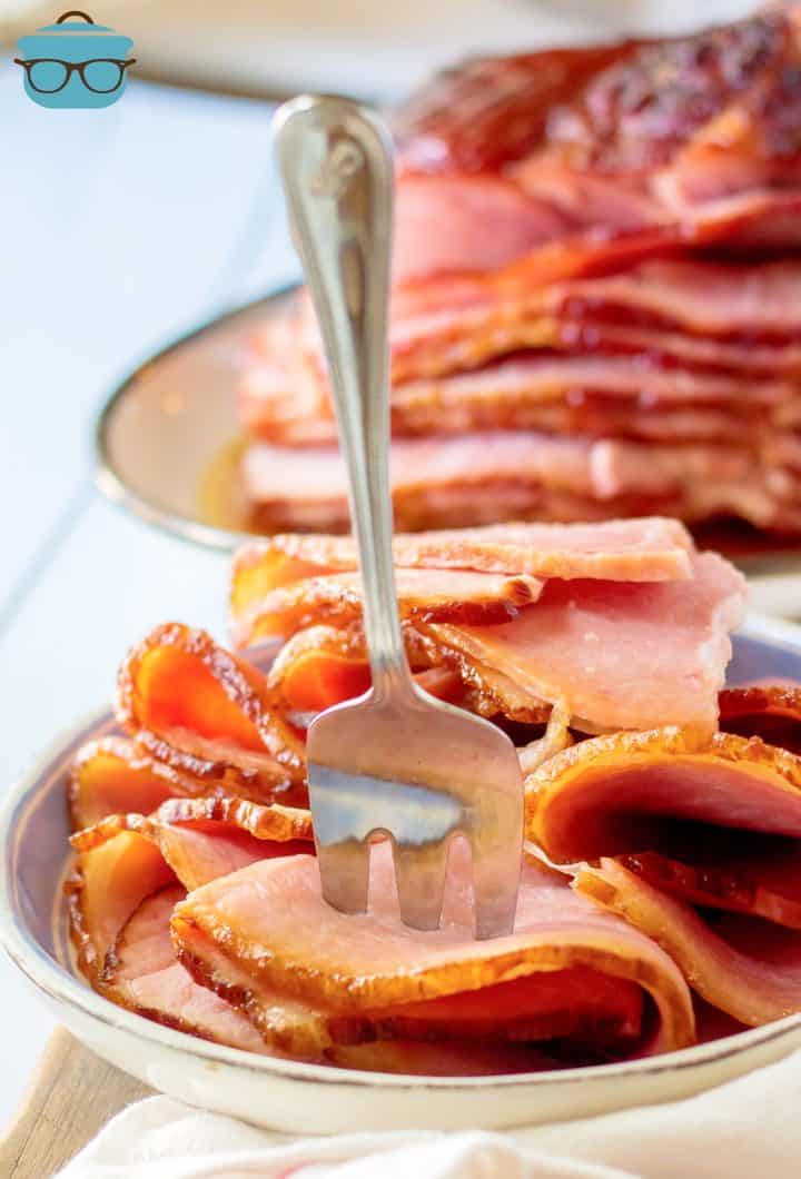Pronged fork in sliced slices of Apple Cider Glazed Ham on plate.