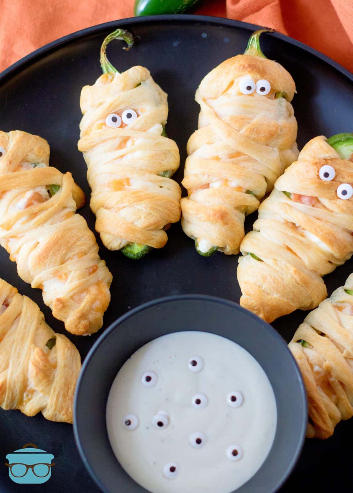 Halloween Mummy Jalapeno Poppers on black plate with dipping sauce.