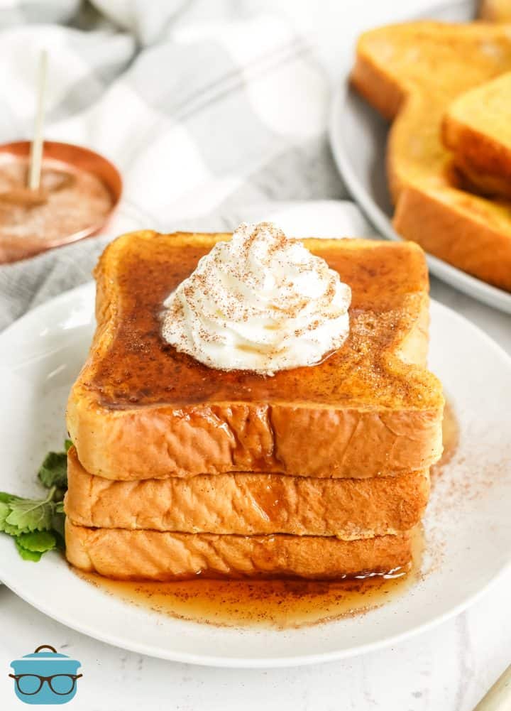 Three slices of Pumpkin French Toast stacked on white plate with whipped topping.