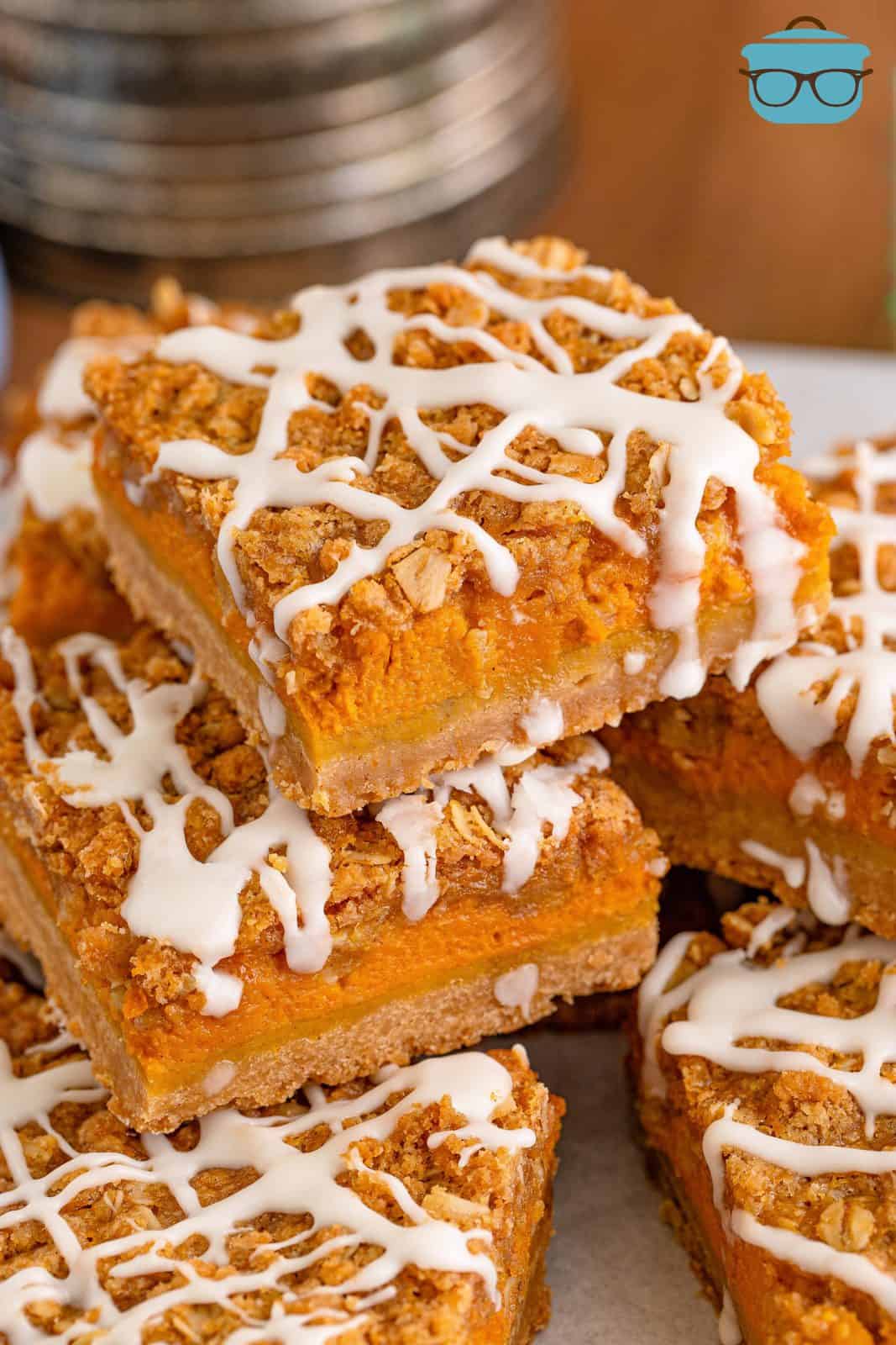 close up photo of a stack of pumpkin streusel bars on white parchment paper. 