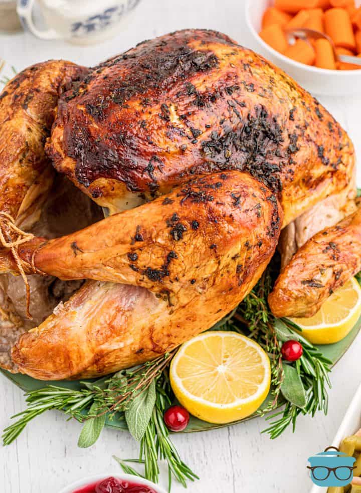 Finished Easy Roast Turkey Recipe on platter with herbs and lemons.