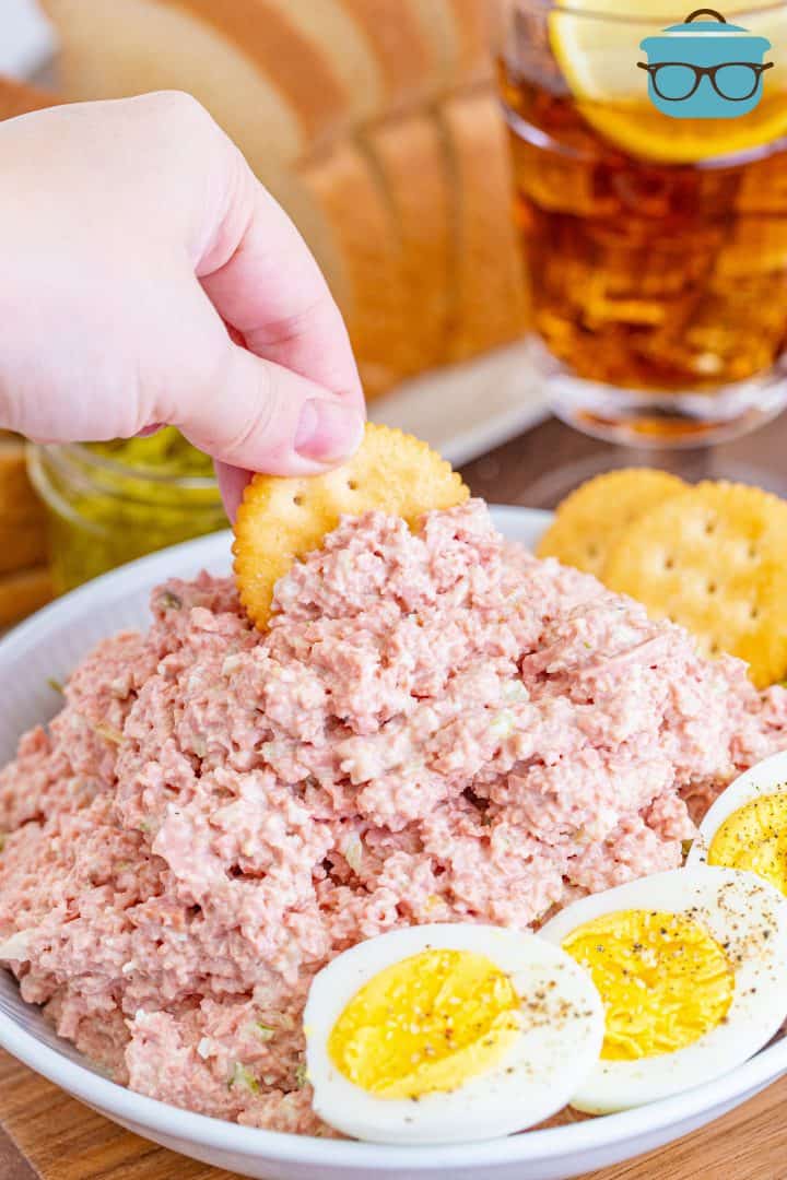 Old-Fashioned Bologna Salad in bowl with hand dipping a cracker into salad.