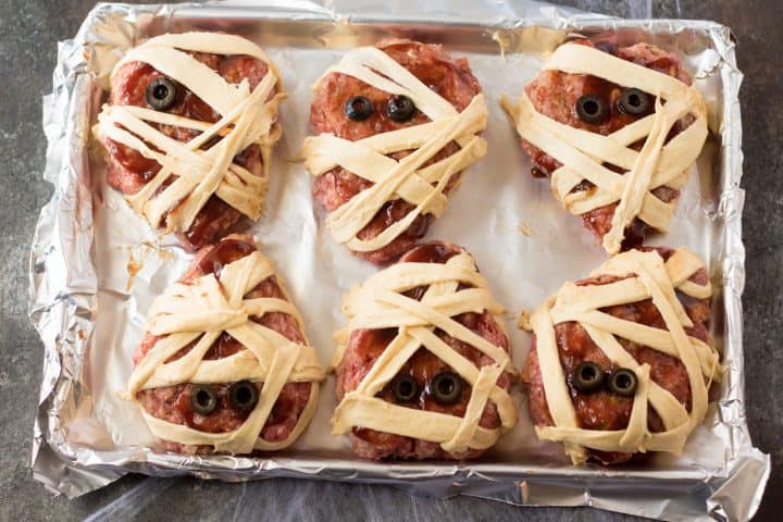 Meatloaf patties wrapped in strips of crescent rolls and black olives placed as eyes.