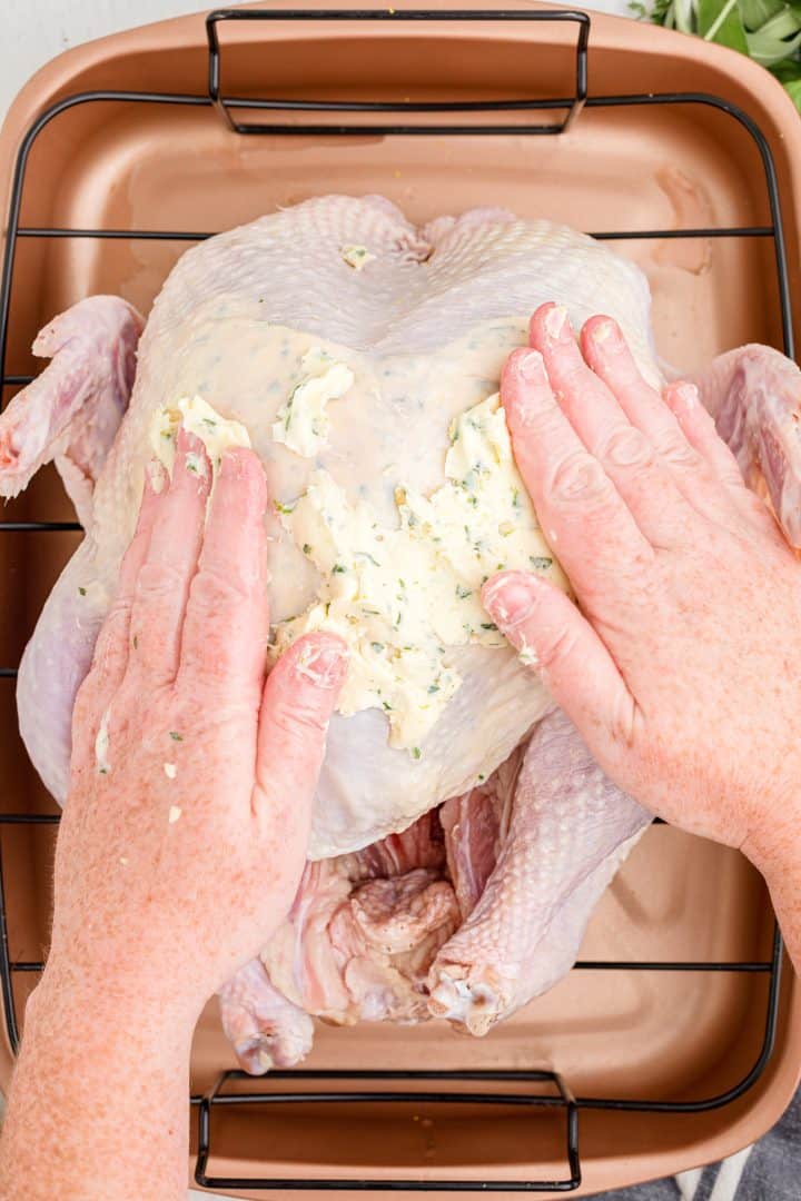 Hands spreading herb butter on turkey.