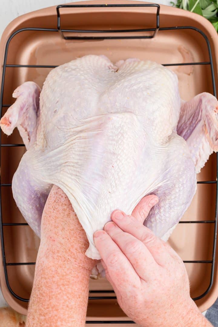 Hand lifting up the turkey skin putting butter under it.