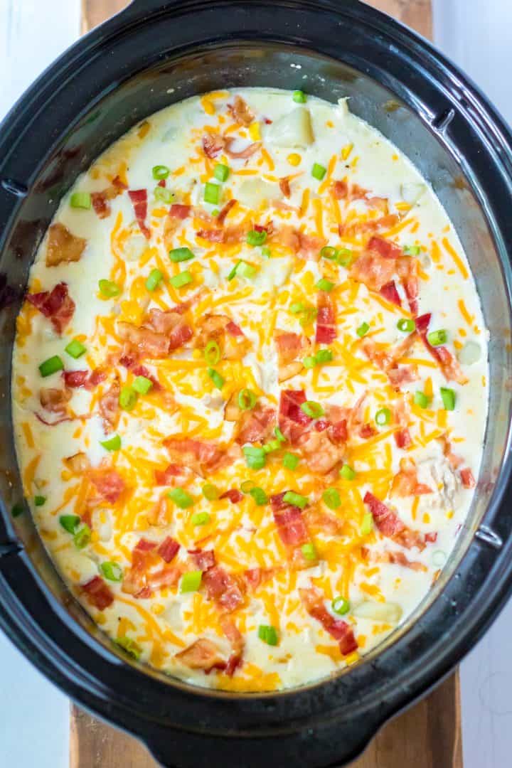 sliced cheese, chopped bacon and sliced green onion shown on top of turkey chowder in the crock pot.