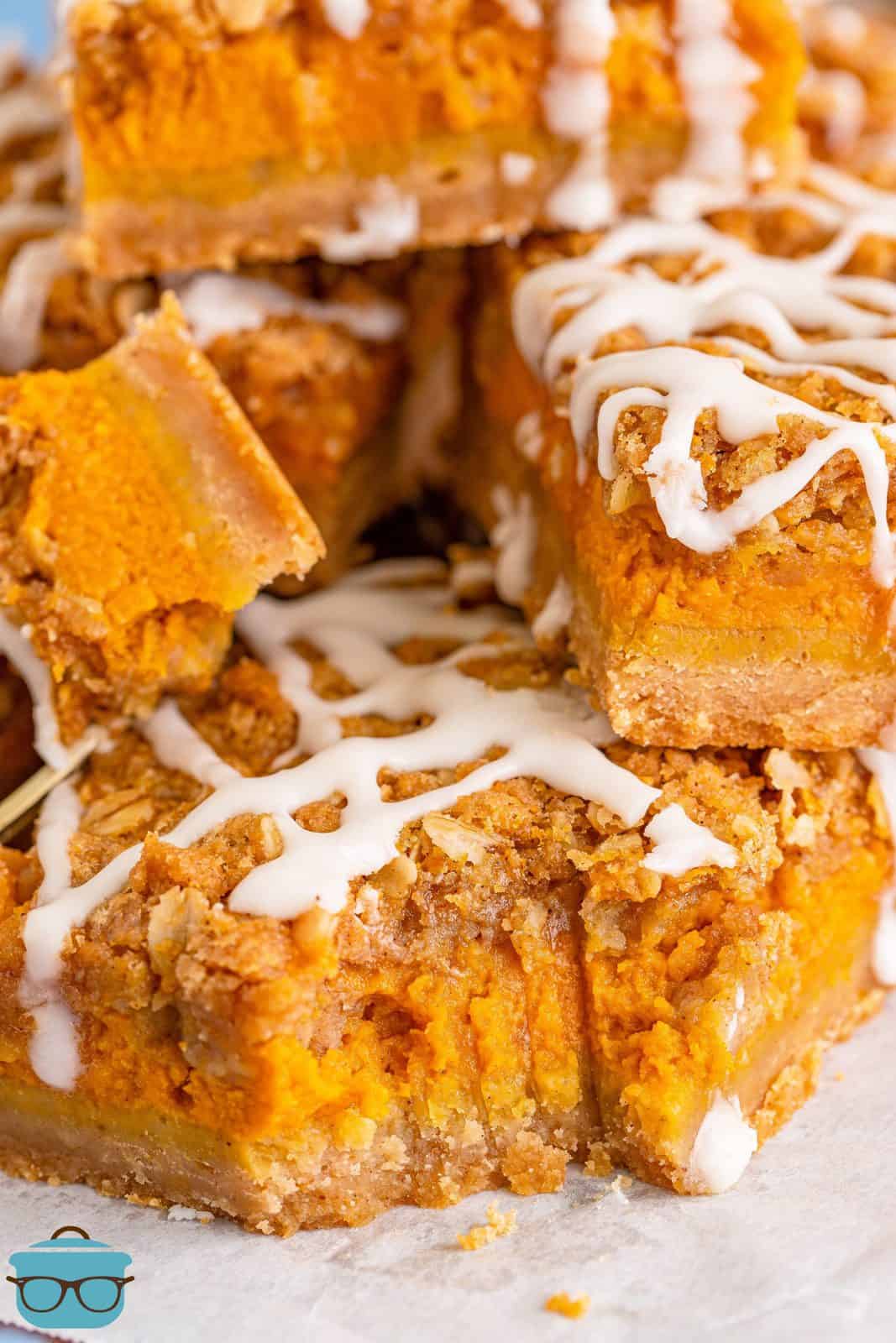 close up photo of pumpkin streusel bars stacked on white parchment paper and a bite removed from one of the bars. 