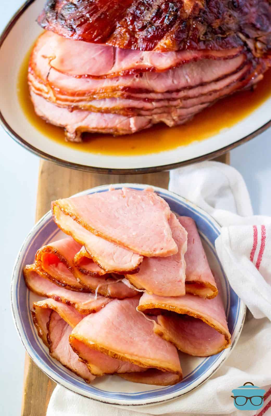 Sliced Apple Cider Glazed ham on white plate with whole ham in background.