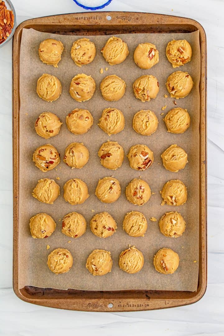 Cookie dough balls on lined baking pan ready to be cillled.