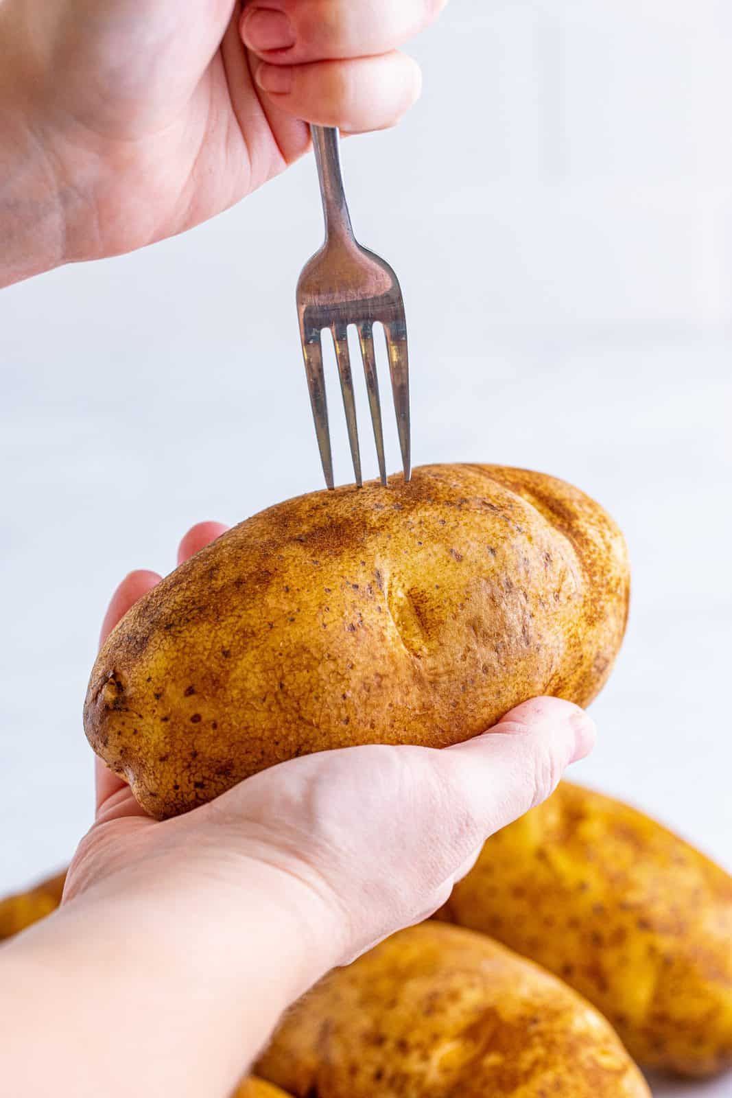 Hand piercing potato with fork.