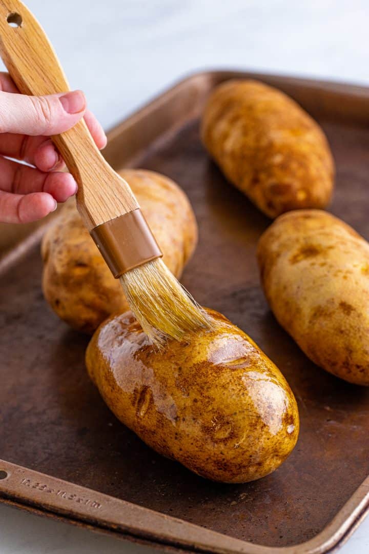Hand brushing potatoes with olive oil.