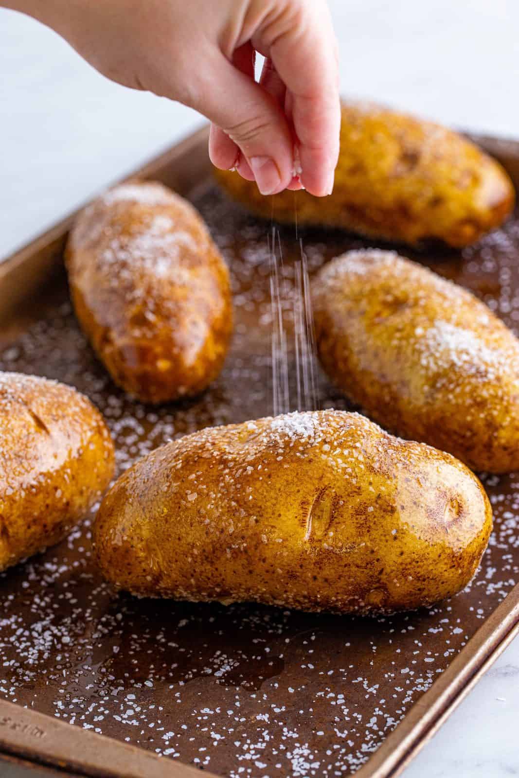 Hand sprinkling salt over potatoes on baking pan.