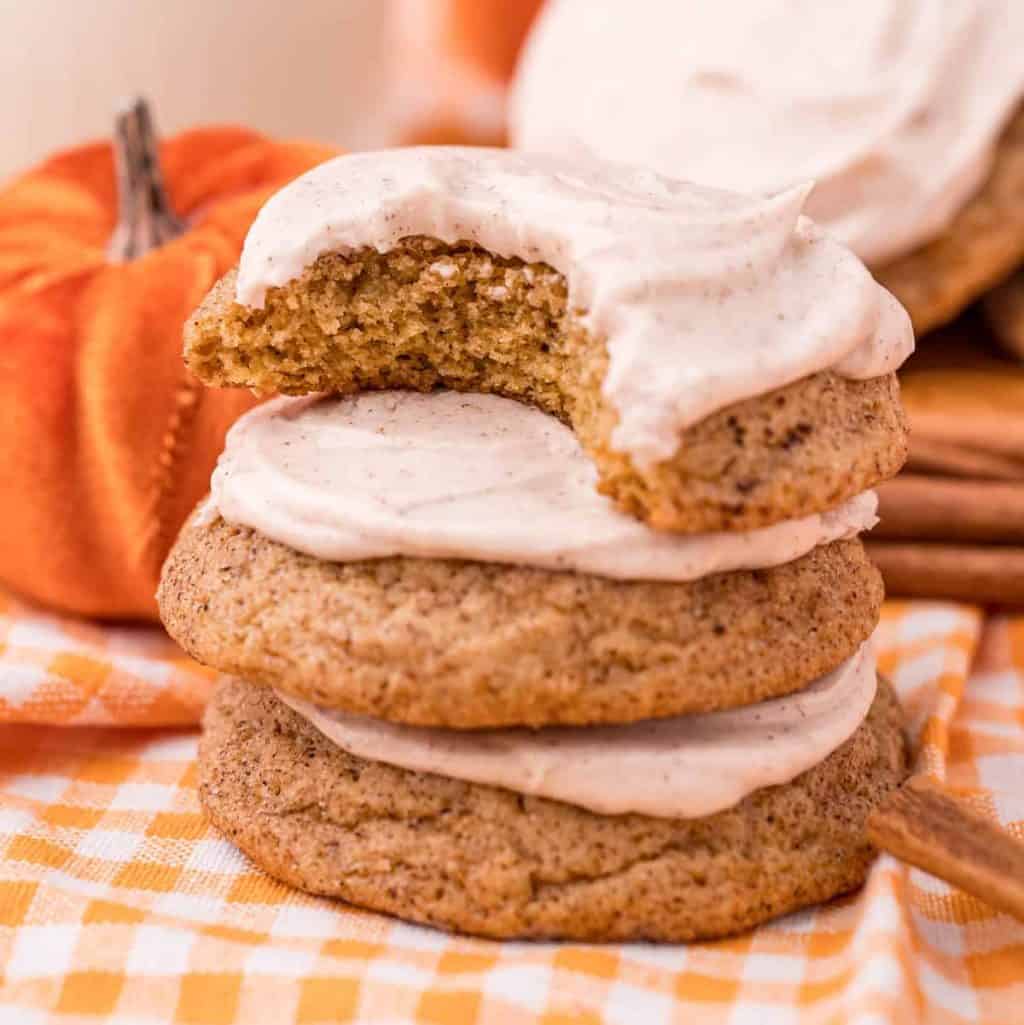Square image of stacked Frosted Pumpkin Cookies with bite taken out of top cookie.