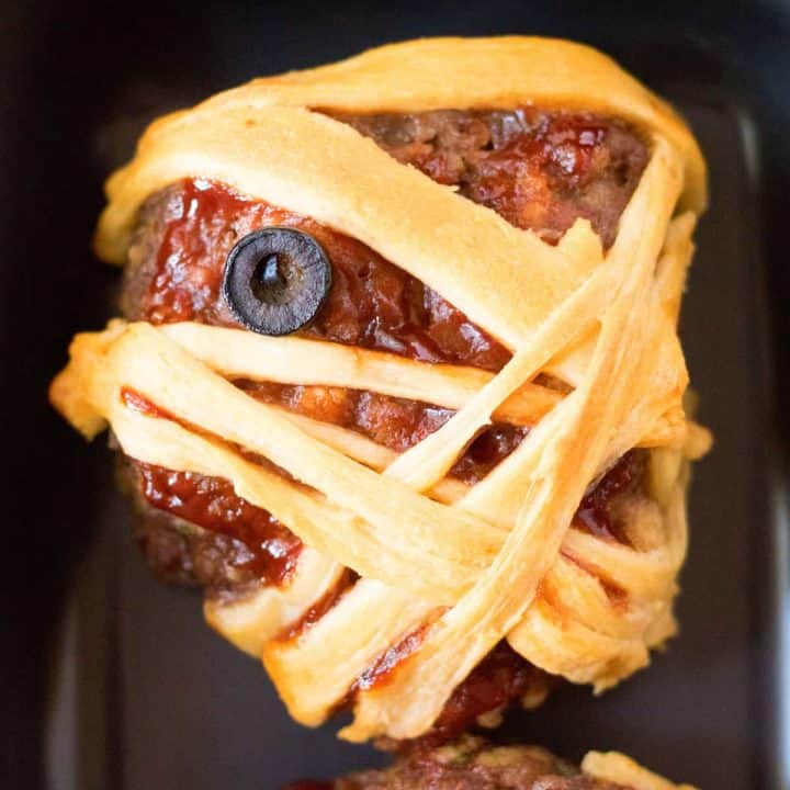 Square image of one baked Halloween Mummy Meatloaf up close on black plate.