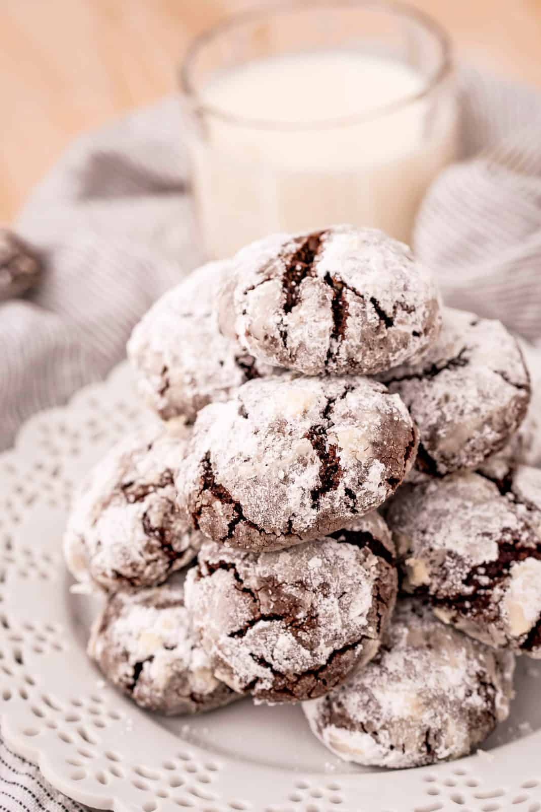 Stacked Chocolate Crinkle Cookies on white plate with milk in background.
