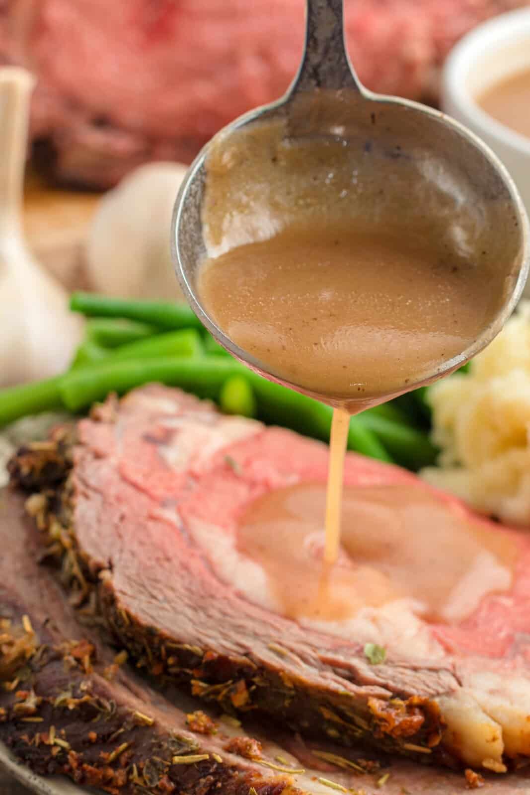 Ladle spooning au jus over slice of Garlic Butter Prime Rib.
