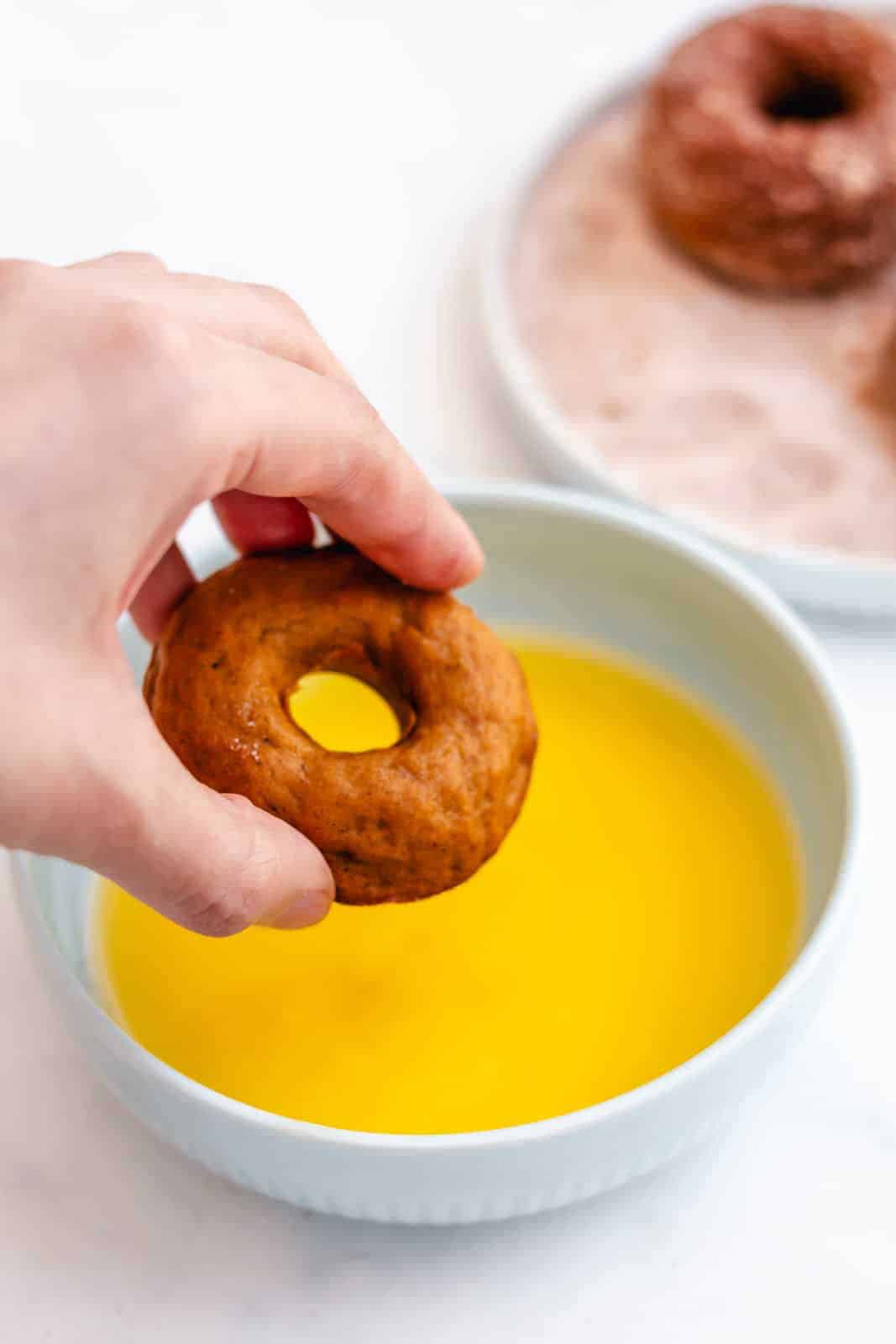 Hand dipping donuts in melted butter.