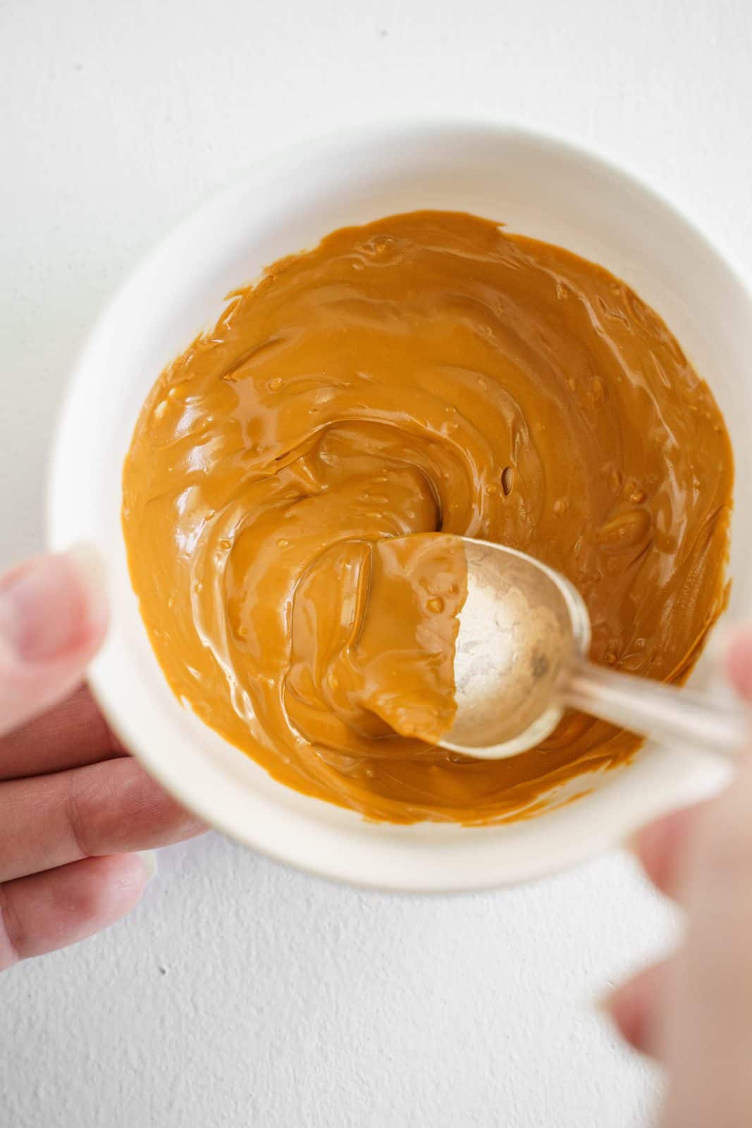 Spoon stirring melted peanut butter candy melts in white bowl.