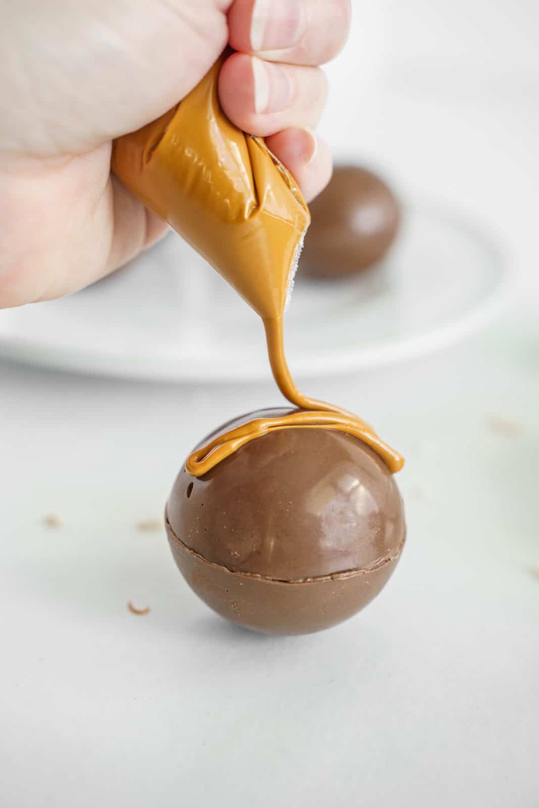 Peanut butter candy melts being piped over Hot Cocoa Bomb
