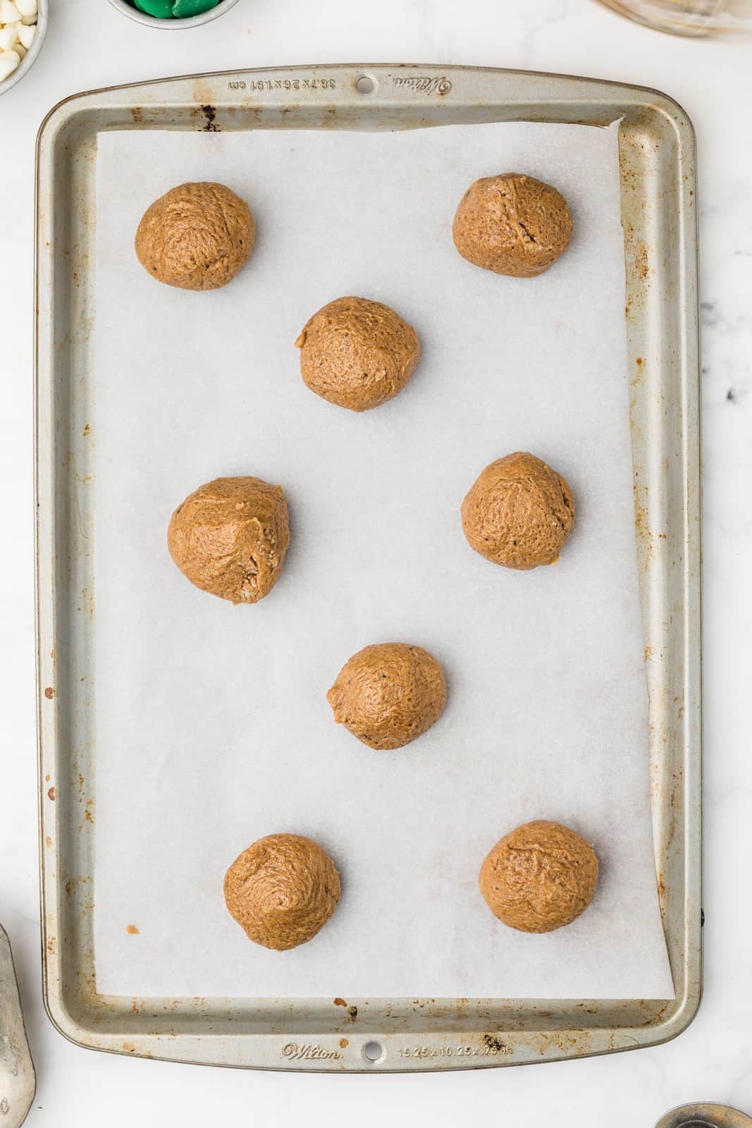 Cookies rounded into balls on parchment lined baking sheet.